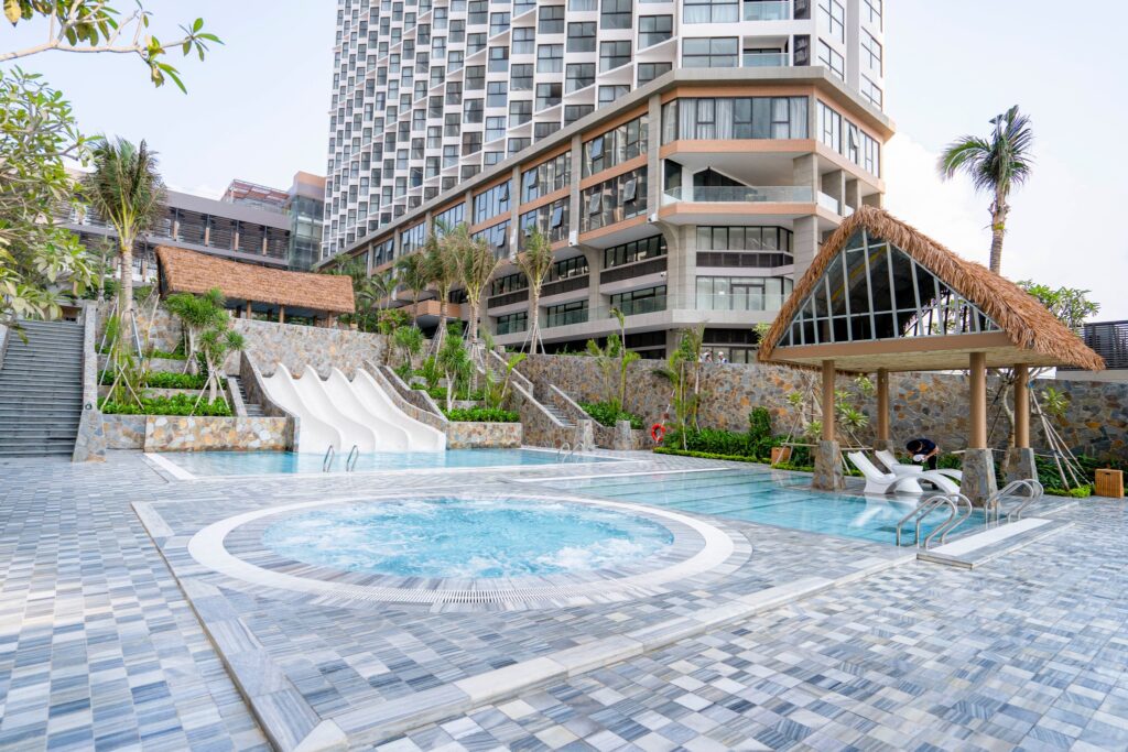 Khu vực hồ massage và trượt nước trong resort với chòi nghỉ lợp mái lá nhân tạo cạnh tòa nhà cao tầng hiện đại